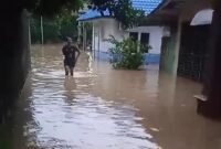 Seorang wanita tengah melintasi jalan yang terendam banjir di Kota Binjai