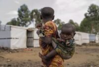 Seorang gadis muda menggendong saudara perempuannya berdiri di luar kamp pengungsi di pinggiran Goma, Republik Demokratik Kongo. Penyakit misterius sedang berjangkit di Kongo. (AP Photo/Moses Sawasawa)