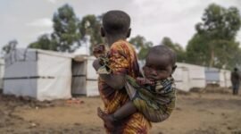 Seorang gadis muda menggendong saudara perempuannya berdiri di luar kamp pengungsi di pinggiran Goma, Republik Demokratik Kongo. Penyakit misterius sedang berjangkit di Kongo. (AP Photo/Moses Sawasawa)